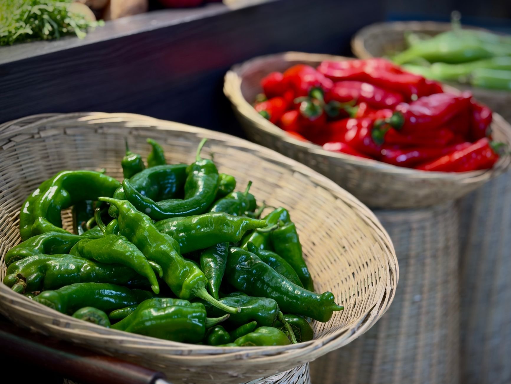 Fresh red and green peppers in woven baskets at a local market